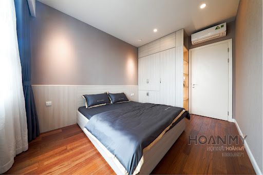 Không gian đơn giản với nội thất gỗ: giường ngủ, tủ đầu giường và tủ quần áo.